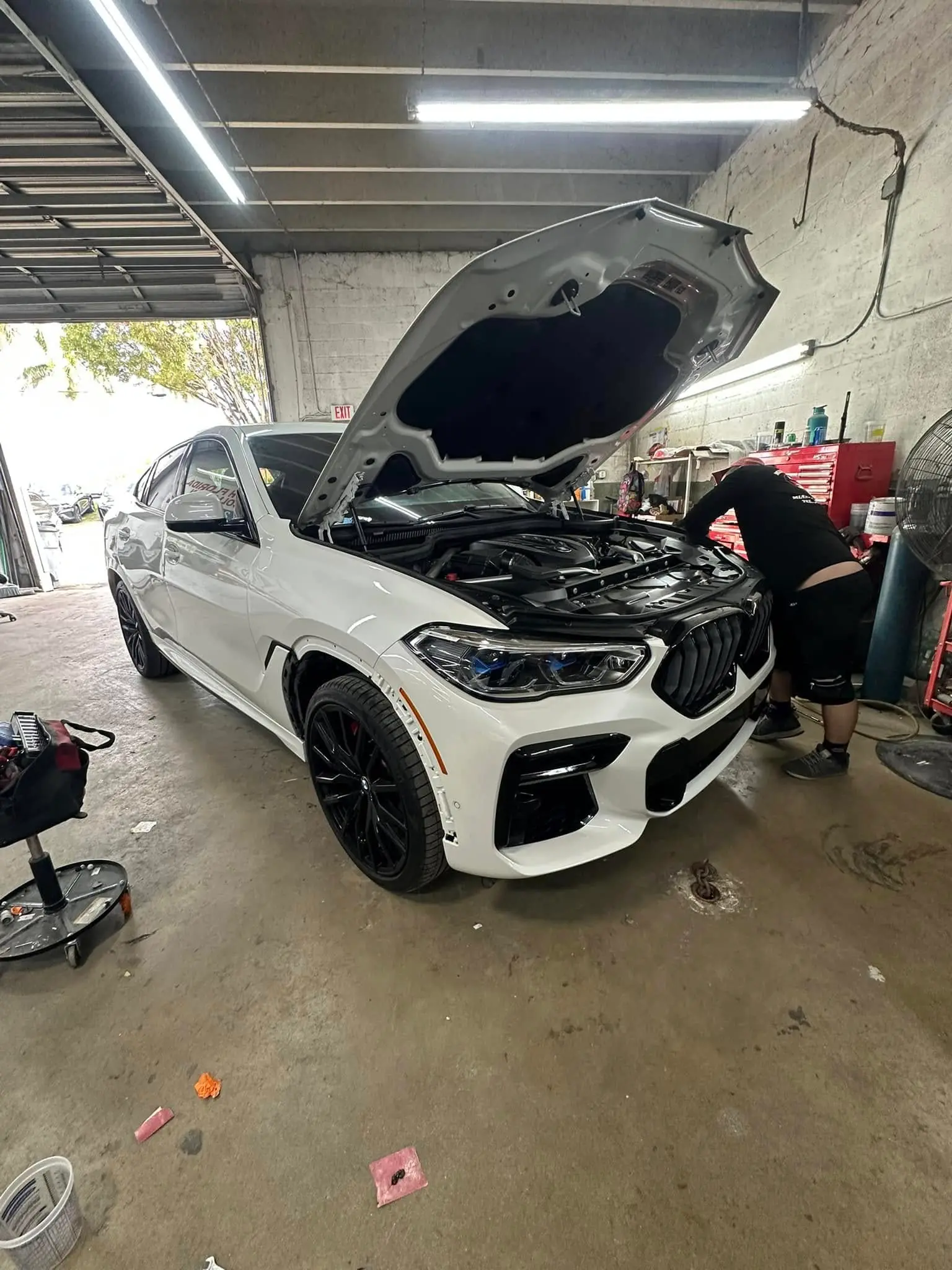 White BMW X6 with the hood open while a technician works on it at Marlin Motors in Cutler Bay, FL